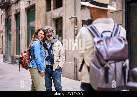 Young male photographer taking holiday photo happy elderly tourist couple posing smile city street Stock Photo