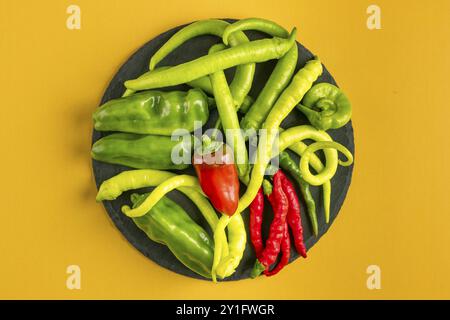 Various green and red peppers on a round plate against a yellow background Stock Photo