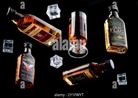 Four whisky bottles and a glass of whisky between floating ice cube cubes against a black background Stock Photo