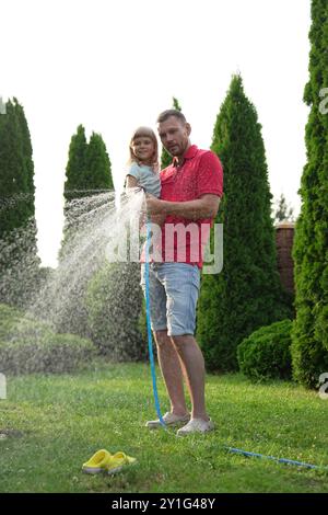 Father and his daughter watering lawn with hose in backyard Stock Photo