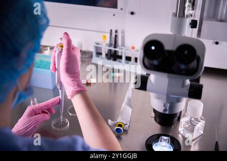Scientist using a pipette near a microscope Stock Photo