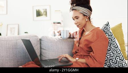Happy woman, coffee and relax with laptop on sofa for online browsing, research or app at home. Young, female person or vlogger with caffeine or Stock Photo