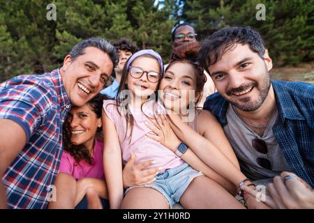 Joyful multigenerational family and friends taking a selfie in a natural setting. Diverse group of adults, children, and seniors smiling and embracing Stock Photo