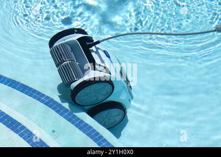 Robotic pool cleaner with a long hose cleaning the bottom of a clear blue swimming pool on a sunny day underwater Stock Photo