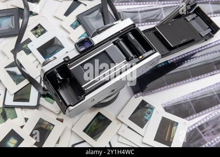 A vintage SLR photo camera with its back cover opened together with a pile of slides and film negatives. Stock Photo