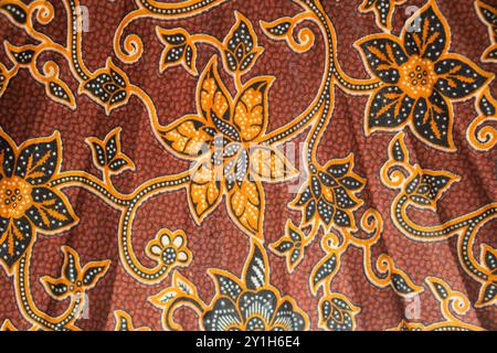 A close-up of intricate batik fabric featuring floral patterns in orange, black, and brown hues. The design showcases detailed flowers and vines, crea Stock Photo