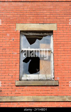 Boarded up broken window with white painted rotten wooden window frame, stone lintel and window head and red brick, in radcliffe greater manchester uk Stock Photo