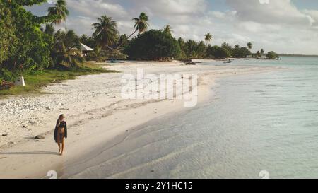 Young woman is enjoying a peaceful walk along a pristine white sand beach, surrounded by the turquoise waters and lush greenery of a tropical paradise in maupiti island, french polynesia Stock Photo