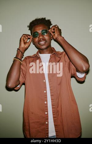 Young handsome man dressed in casual clothes and adjusting turquoise sunglasses posing for portrait Stock Photo