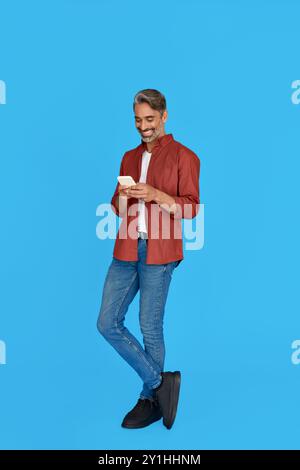 Smiling middle aged man using mobile phone isolated on blue background. Stock Photo