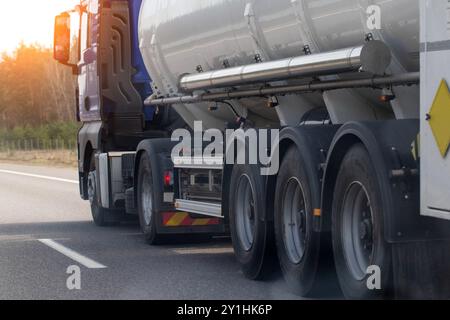 A tanker semi-trailer truck transports a dangerous cargo of gasoline, diesel fuel and petroleum products on the road against the backdrop of the sun. Stock Photo