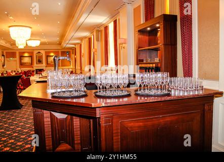 A beautifully arranged bar area with multiple trays of sparkling glasses, set in an elegant banquet hall. The warm lighting and luxurious decor create Stock Photo