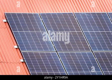 Close-up of solar panels installed on a red corrugated roof for renewable energy generation Stock Photo