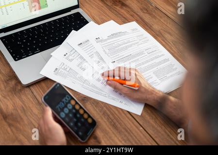 Male company accountant engages in filling tax forms correctly using calculator on smartphone Stock Photo
