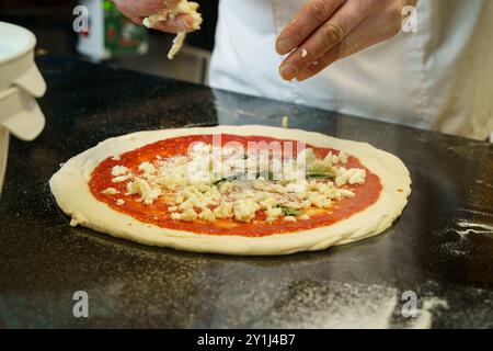 A chef preparing a pizza with tomato sauce and spreading mozzarella cheese on pizza Stock Photo