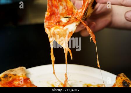 Taking a slice of salami pizza with melted cheese Stock Photo