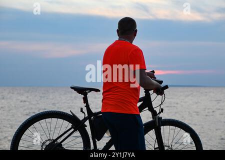 Cyclist with his bike is taking a break at sunset on the beach after a bike ride. Stock Photo