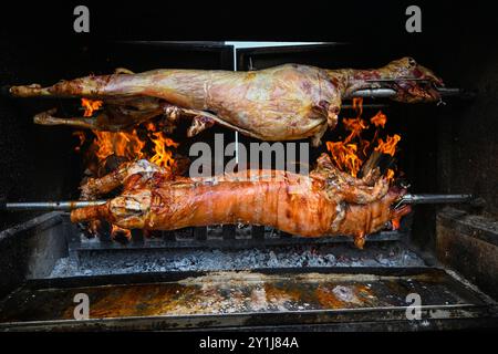 Whole lamb and pig are roasting on a spit over a fire pit. Stock Photo