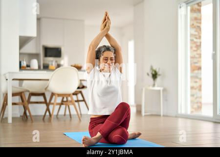 Happy healthy fit older woman doing yoga exercises sitting at home. Stock Photo