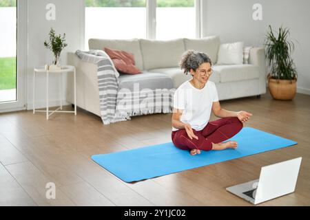 Happy healthy mature woman doing morning exercises with online tutorial at home. Stock Photo