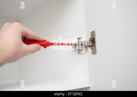 A worker installs a furniture hinge on the door of a wardrobe Stock Photo