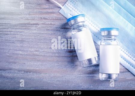 Medication in glass vials with blank labels and medical mask on wooden table, flat lay. Space for text Stock Photo