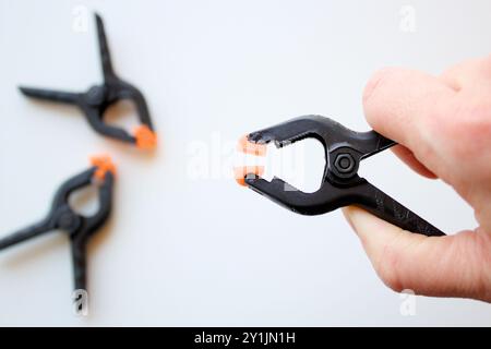 Caucasian hand holding a plastic spring clamp over white background. Small heavy duty clips for crafts, backdrop stand, woodwork and industry. Stock Photo