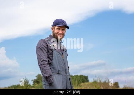 Worker in overalls smiling outdoors in rural area. Working professions. Water supply specialist. Stock Photo