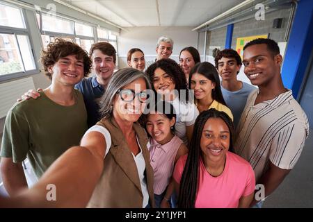 Cheerful selfie of young group of students taking a photo with their teacher in the classroom. Stock Photo