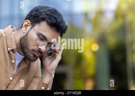Young man wearing glasses with hand to head showing stress and contemplation. Personality captured in thoughtful moment, reflecting feelings of concern or anxiety. Stock Photo