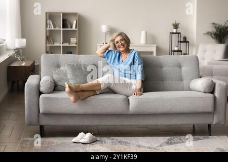 Happy woman wears casual clothes relaxing seated on cozy sofa Stock Photo