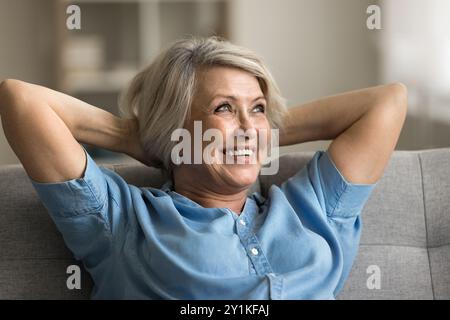 Smiling older woman wearing casual blouse relaxing leaned on couch Stock Photo