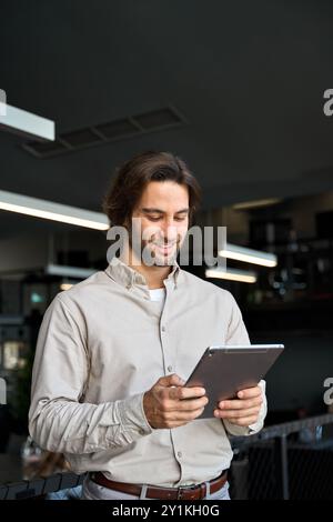 Smiling busy young European business man using tablet standing in office. Stock Photo