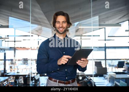 Confident happy young business man entrepreneur holding tab standing in office. Stock Photo