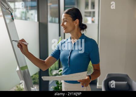 A professional woman writes on a whiteboard in a modern office to convey her ideas clearly Stock Photo