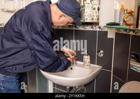 The mature plumber changing the  faucet  using work tool pliers, close-up photo. Plumbing, repairing, assemble concept. Stock Photo