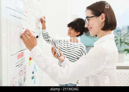 Developing UI design. Women drawing website wireframe on whiteboard indoors Stock Photo
