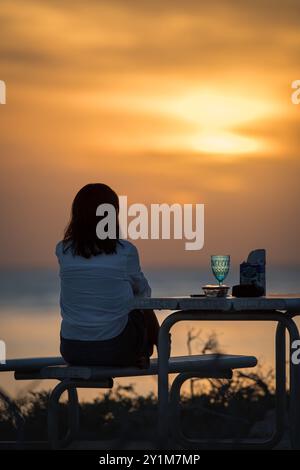 A relaxed ecotourists silhouetted by the setting sun enjoying a happy hour drink over the Indian Ocean at Osprey Bay, Cape Range National Park in WA. Stock Photo