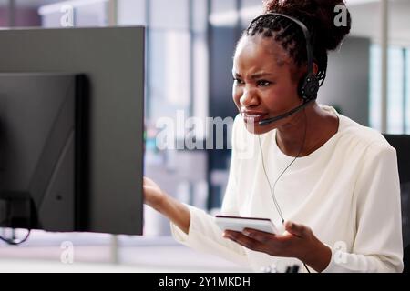 Worried African American businesswoman in office uses headset for video conference, stressed about cyber attack and data protection. Stock Photo