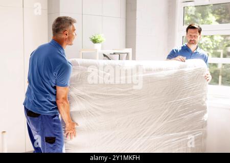 Skilled movers showcasing teamwork and interior decoration by delivering a new mattress to a bedroom in a real estate rental. Stock Photo