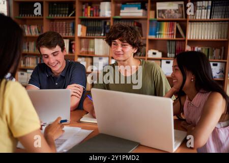 Group of students gathered in the library to work together on a school project, using laptops. Stock Photo