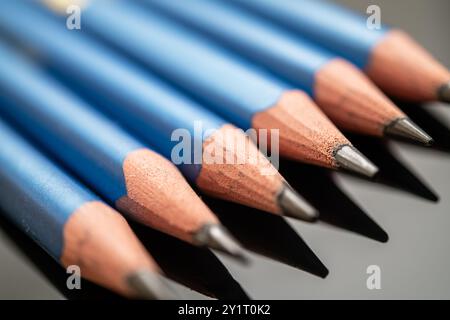 Blue colored pencils with sharpened tips arranged neatly in a row, reflecting on a glossy black surface. Suitable for art, education, and creative pro Stock Photo