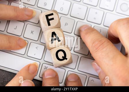 The phrase FAQ on wooden cubes. White computer keyboard with people's hands asking questions. Frequently asked questions Stock Photo