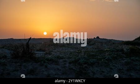 A sunset casts vibrant colors over a grassy field with a fence Stock Photo
