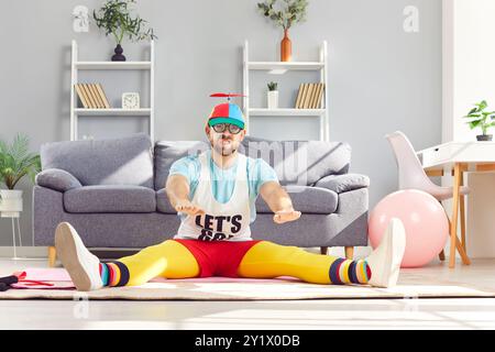 Funny man doing stretching exercises sitting on the floor in living room at home. Stock Photo