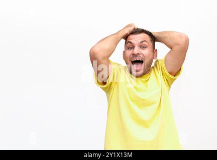 Young man in yellow t-shirt holds hair in hand and screams with delight, isolated on white background. Stock Photo