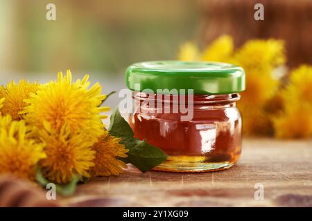 Dandelion honey in a small glass jar with green cap on a table outdoors in nature Stock Photo