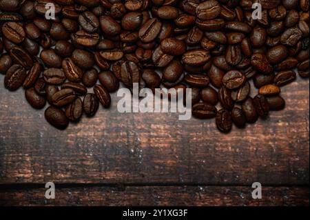 Coffee beans are scattered across a wooden table in this dark, stylish image. The rich texture of the beans contrasts with the rustic wood surface. Stock Photo