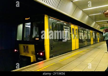 A yellow and black metro train arriving at an underground station with passengers waiting. Stock Photo