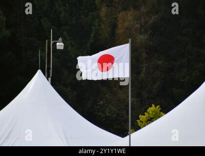 The national flag of Japan flying in the breeze up a flagpole between two white tents. Stock Photo